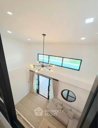 Spacious living room with high ceiling and modern chandelier, featuring large windows and elegant decor.