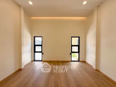 Spacious empty room with wooden flooring and modern windows, perfect for customization.