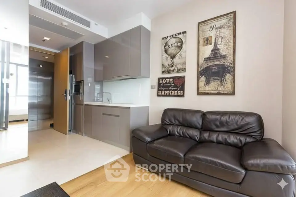 Modern living room with sleek kitchen, leather sofa, and stylish wall art in a contemporary apartment.