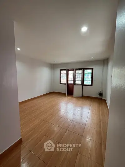 Spacious empty room with wooden flooring and large windows for natural light.