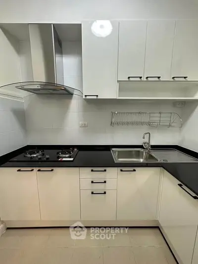 Modern kitchen with sleek black countertops and white cabinetry, featuring a gas stove and stainless steel sink.