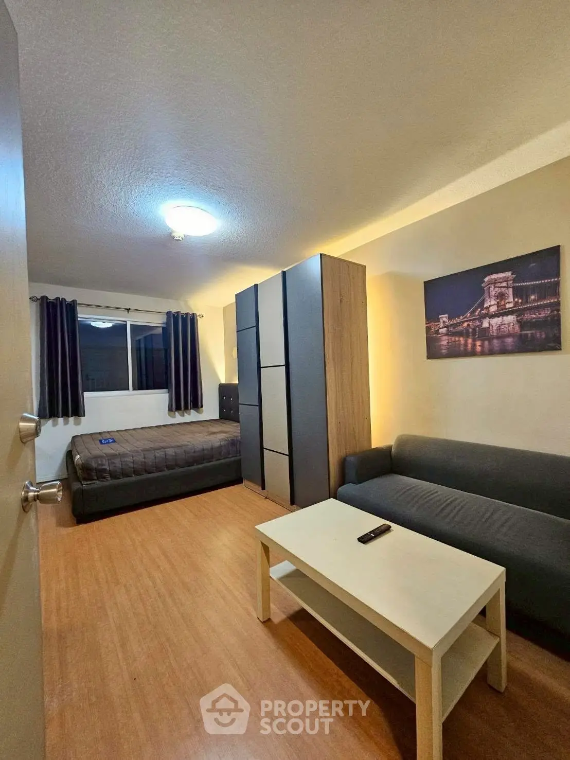 Cozy studio apartment with modern furnishings and wooden flooring, featuring a comfortable bed and stylish sofa.
