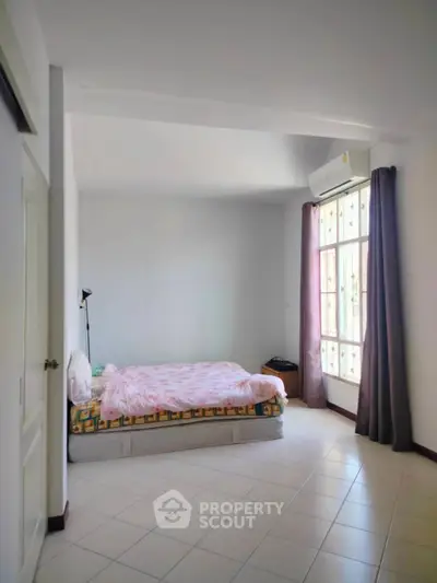Spacious bedroom with natural light and minimalist decor, featuring a cozy bed and large window.