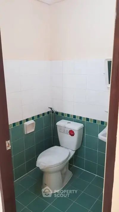 Compact bathroom with green and white tiles, featuring a standard toilet.