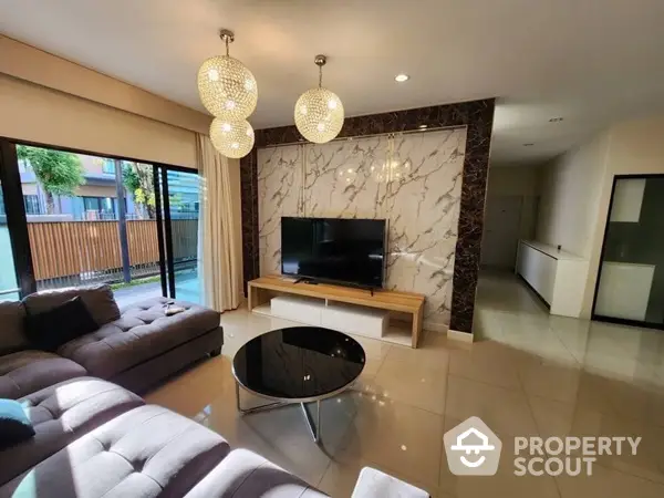 Spacious living room with elegant marble accent wall, modern furniture, and chic pendant lighting, opening to a sunlit patio.