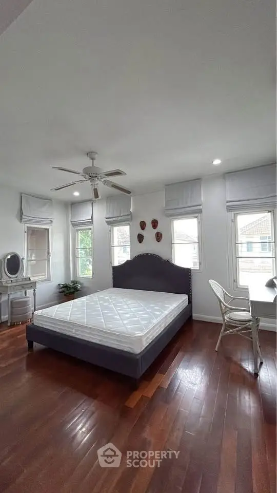 Spacious bedroom with hardwood floors and natural light, featuring a modern bed and ceiling fan.