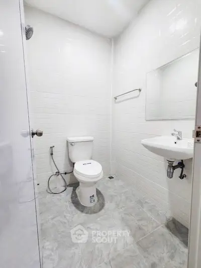 Modern white-tiled bathroom with toilet and sink in minimalist design.