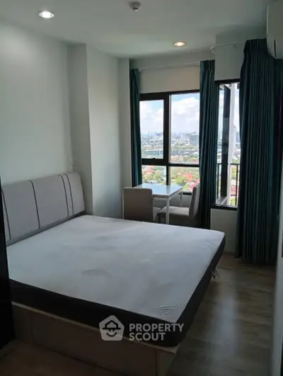 Modern bedroom with city view and natural light, featuring a cozy bed and small dining area.