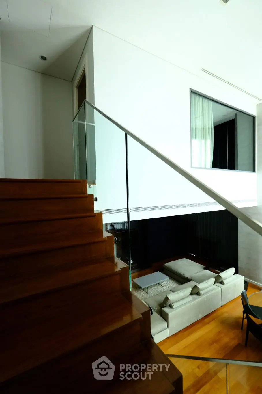 Modern duplex living room with wooden staircase and glass railing