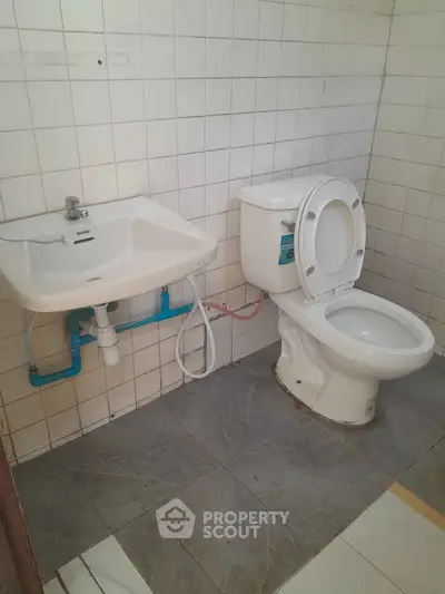 Compact bathroom with white tiles, featuring a toilet and wall-mounted sink, ideal for small spaces.