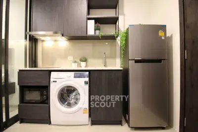 Modern kitchen with washing machine, fridge, and sleek cabinetry in a compact layout.