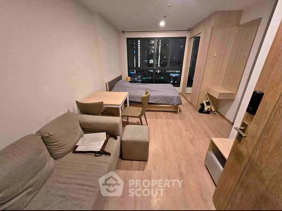 Modern studio apartment with cozy living area and city view, featuring wooden flooring and stylish furniture.