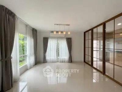 Spacious living room with large windows and elegant curtains, featuring a modern light fixture and sliding glass doors.