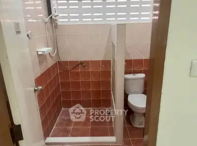 Compact bathroom with shower and toilet, featuring red and beige tiles.
