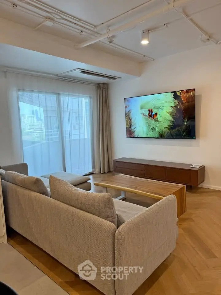 Modern living room with large TV, cozy sofa, and city view from balcony.