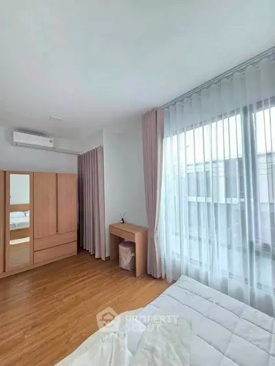 Bright and airy bedroom with large window and wooden flooring, perfect for relaxation.