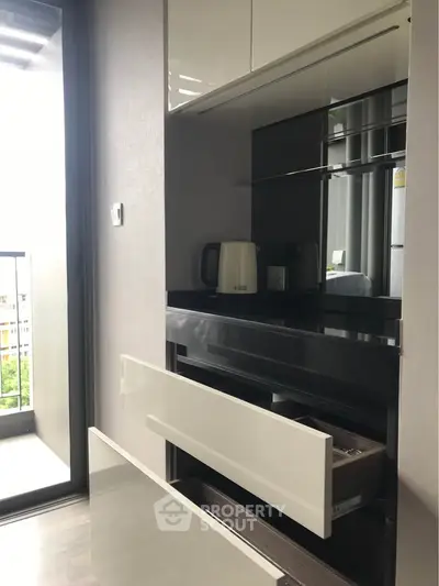 Modern kitchen with sleek cabinetry and balcony view, featuring a kettle and ample storage space.