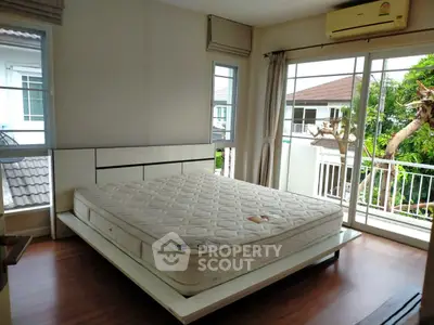Bright bedroom with large windows and balcony access, featuring a modern bed and wooden flooring.