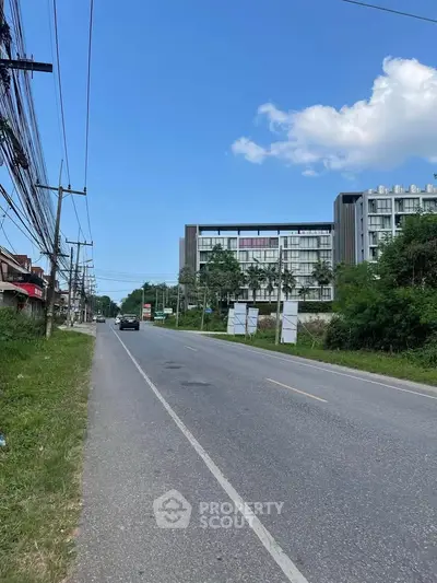 Modern building exterior along a quiet road with lush greenery and clear blue sky.