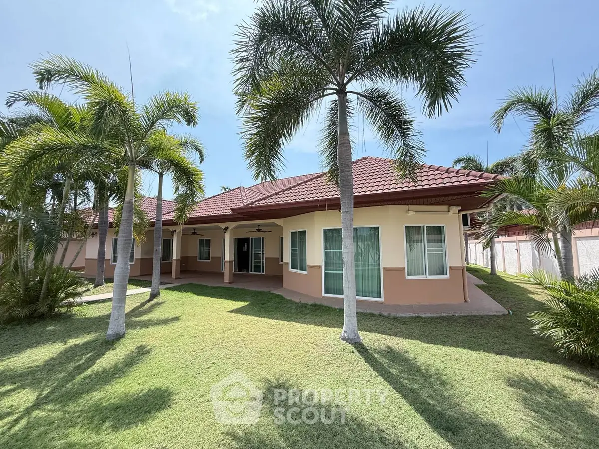 Charming single-story home with red-tiled roof and lush palm trees in a spacious garden setting.
