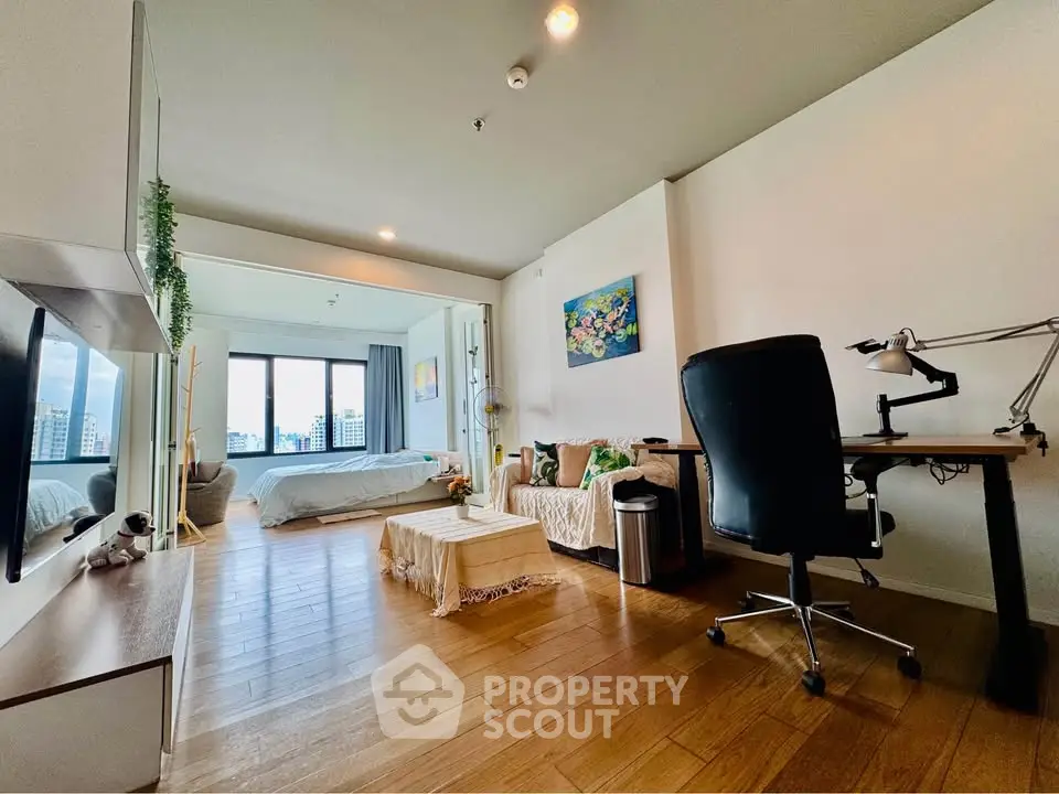 Spacious modern studio with wooden flooring and city view, featuring a cozy living area and work desk.
