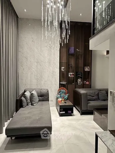 Luxurious modern living room with high ceilings, elegant chandelier, and stylish gray furniture.