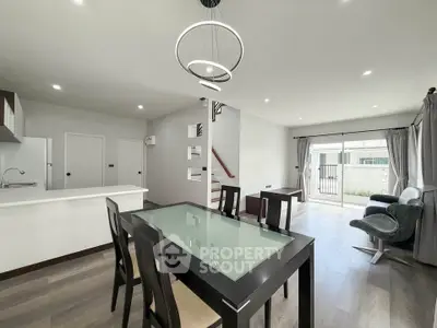 Modern open-plan living room with dining area and sleek kitchen design, featuring contemporary lighting and large windows.