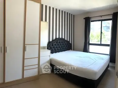 Modern bedroom with striped accent wall and large window for natural light.