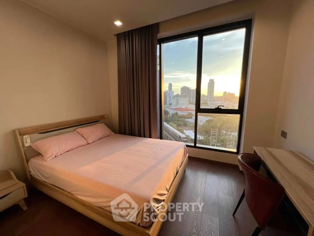 Modern bedroom with city view, featuring a cozy bed and stylish desk, perfect for urban living.