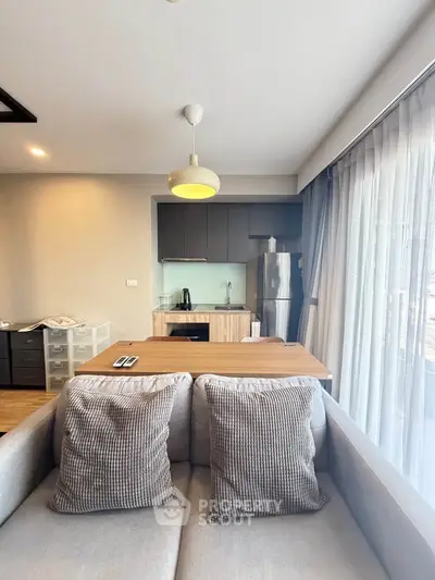 Modern open-plan living room with cozy sofa and sleek kitchen area, featuring large windows for natural light.