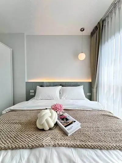 Modern bedroom with elegant decor and natural light, featuring a cozy bed and stylish lighting.