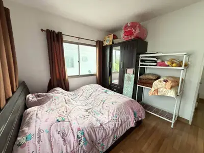 Cozy bedroom with wooden flooring and ample natural light, featuring a large window and stylish storage solutions.