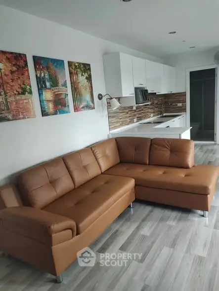 Modern living room with stylish brown leather sectional sofa and sleek kitchen in open layout.