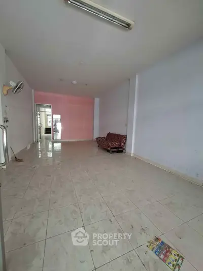 Spacious empty living room with tiled flooring and a single sofa, ideal for customization.