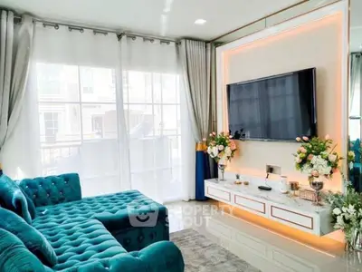 Luxurious living room with teal sofa and large TV, elegant decor and natural light.