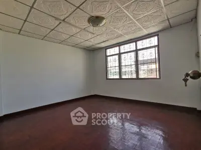 Spacious empty room with polished hardwood floors, ornate ceiling tiles, and large windows allowing ample natural light.