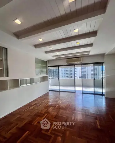Spacious living room with parquet flooring and large windows offering city views.