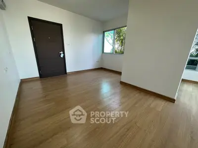Spacious empty room with wooden flooring and large window in modern apartment.