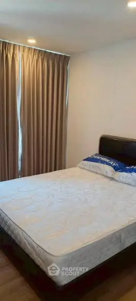 Cozy bedroom with large window and elegant curtains, featuring a comfortable bed and wooden flooring.