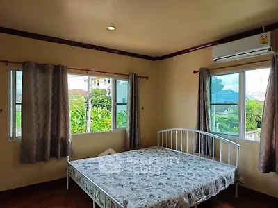 Cozy bedroom with large windows and air conditioning, offering a serene view of greenery.