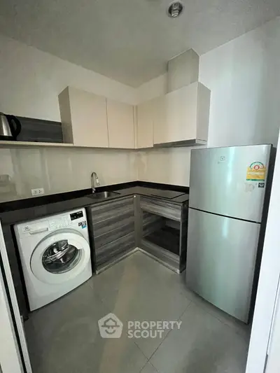 Modern kitchen with sleek cabinets, washing machine, and stainless steel fridge in compact layout.