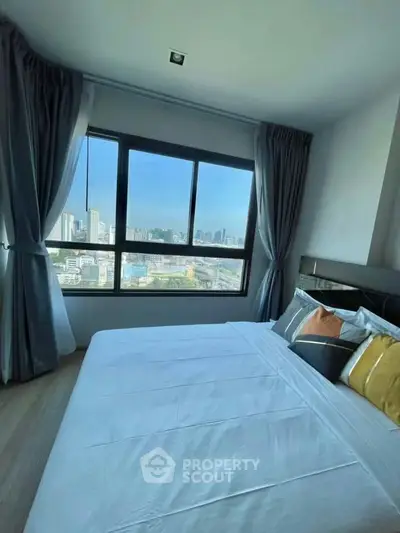 Spacious bedroom with large window offering stunning city view, modern decor and cozy ambiance.