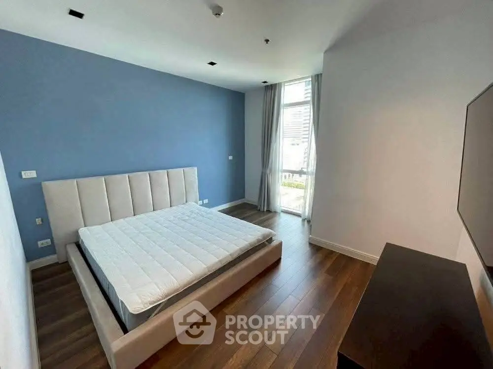 Spacious modern bedroom with large window and hardwood floors in a stylish apartment.
