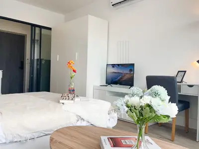 Modern bedroom with cozy decor, featuring a desk, TV, and stylish furnishings in a bright, inviting space.