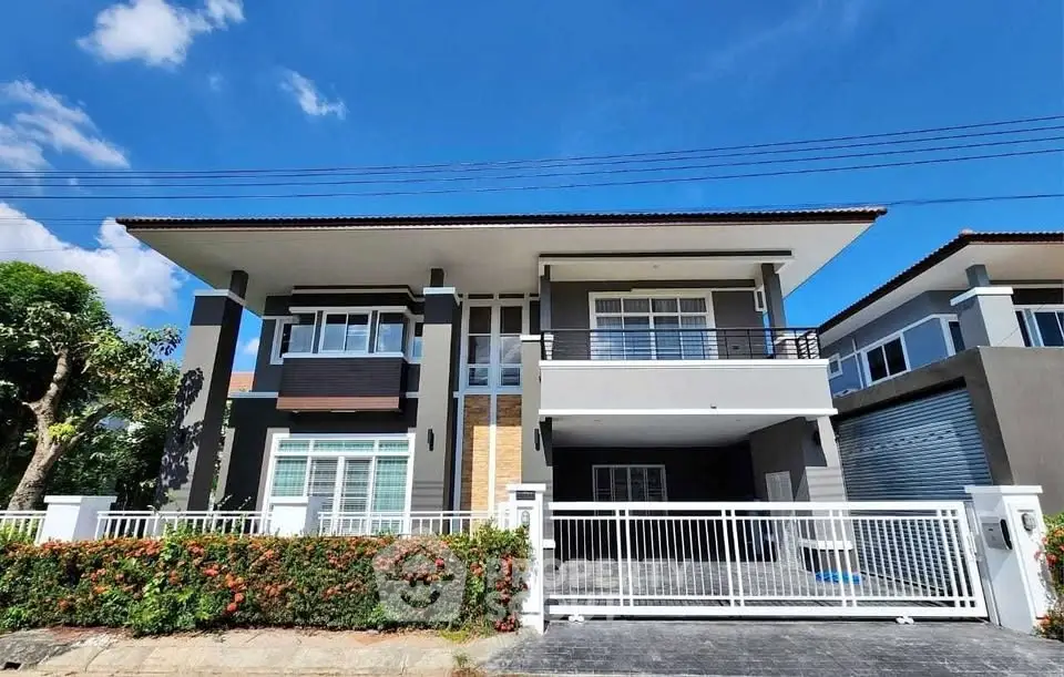 Modern two-story house with spacious balcony and sleek design under clear blue sky.