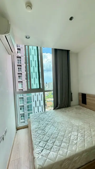 Modern bedroom with large window offering stunning city view in high-rise apartment.