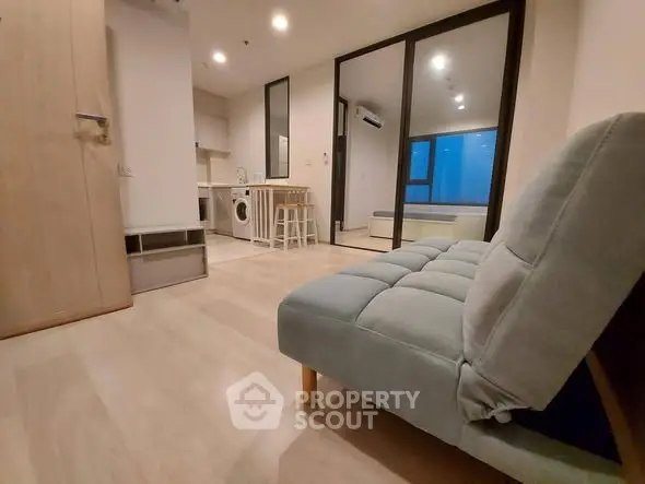 Modern apartment interior with cozy living area and kitchen featuring washing machine and bar stools.