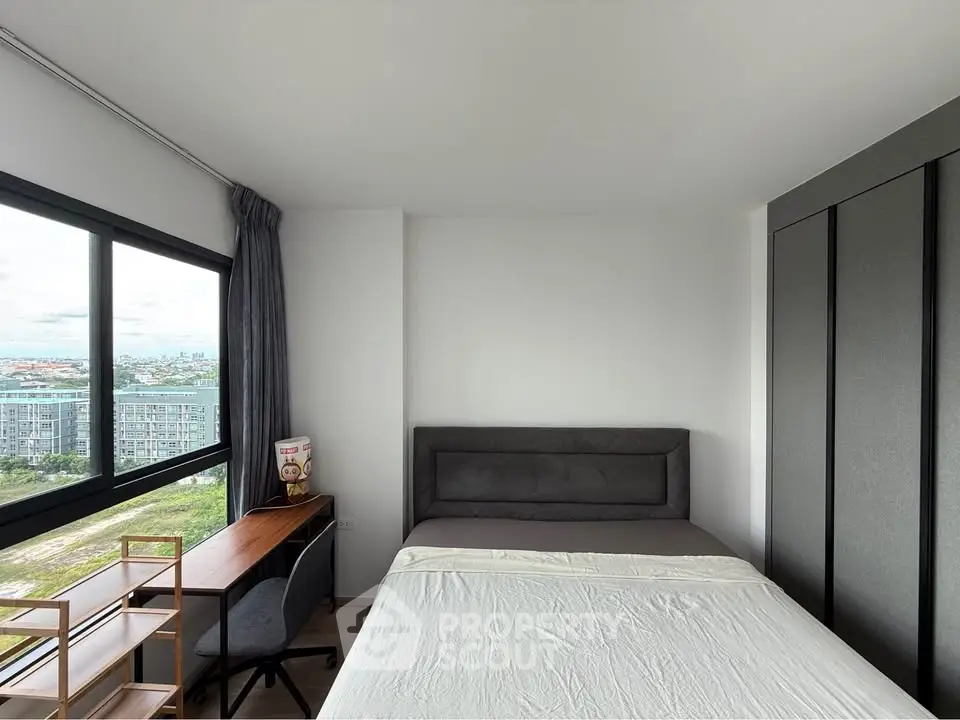 Modern bedroom with large window offering stunning city views, featuring a cozy bed and stylish workspace.