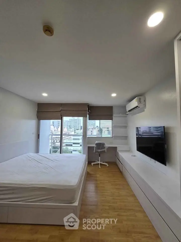 Modern bedroom with city view, featuring sleek furniture and ample natural light.