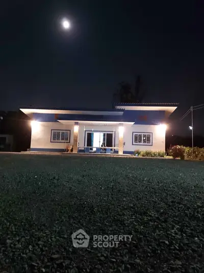 Charming single-story home with illuminated facade under a moonlit sky, surrounded by a spacious lawn.